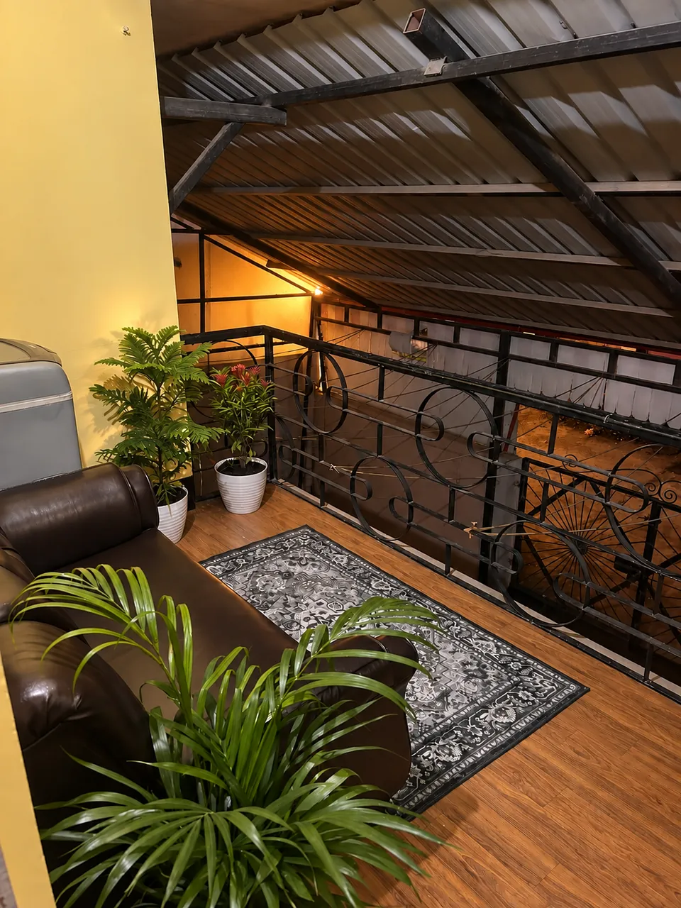 Balcony at night with a leather sofa, rug, plants and a wrought-iron railing