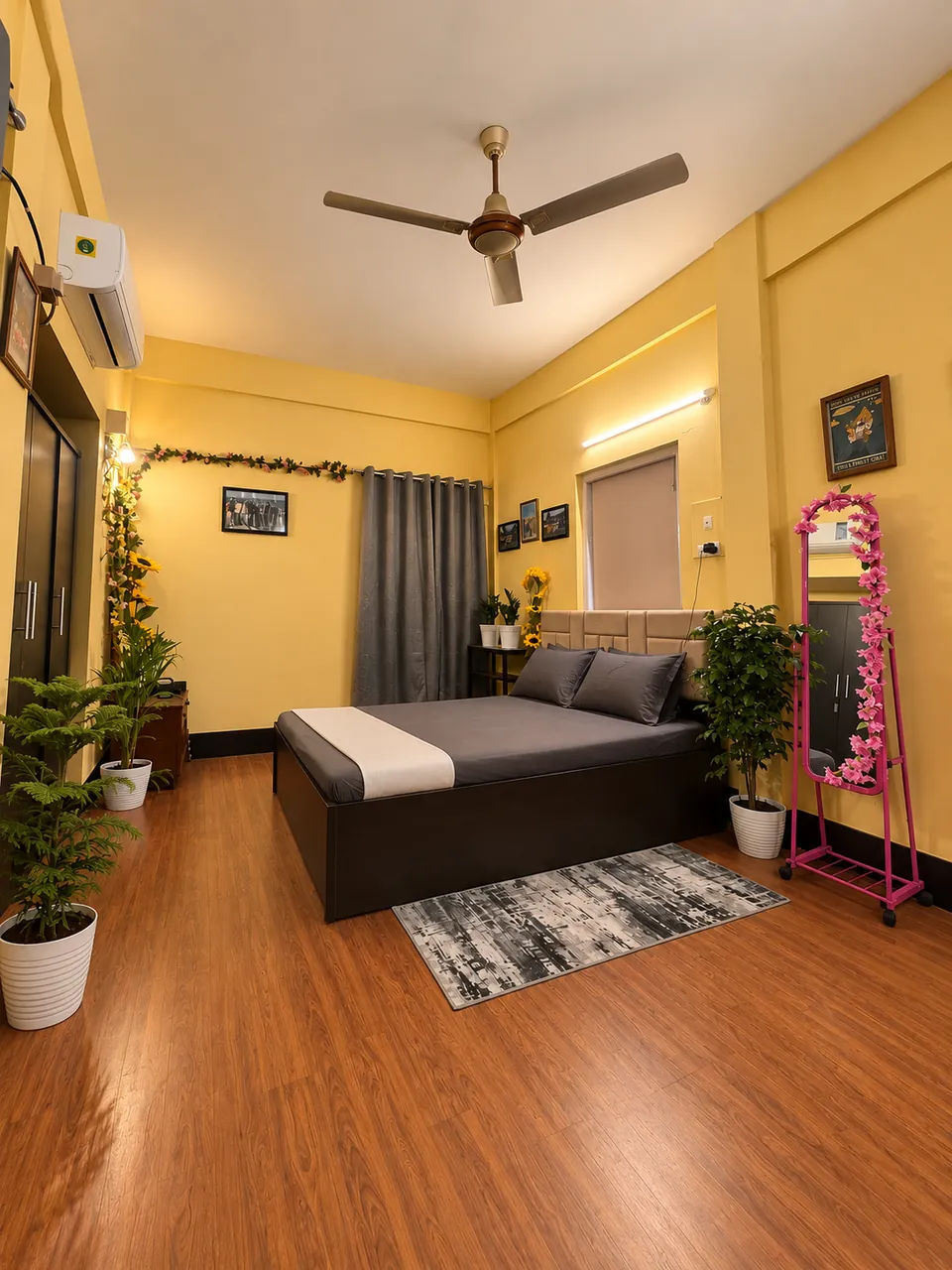 Bedroom 1 with a queen bed, grey bedding, an air conditioner, plants and a full-length mirror